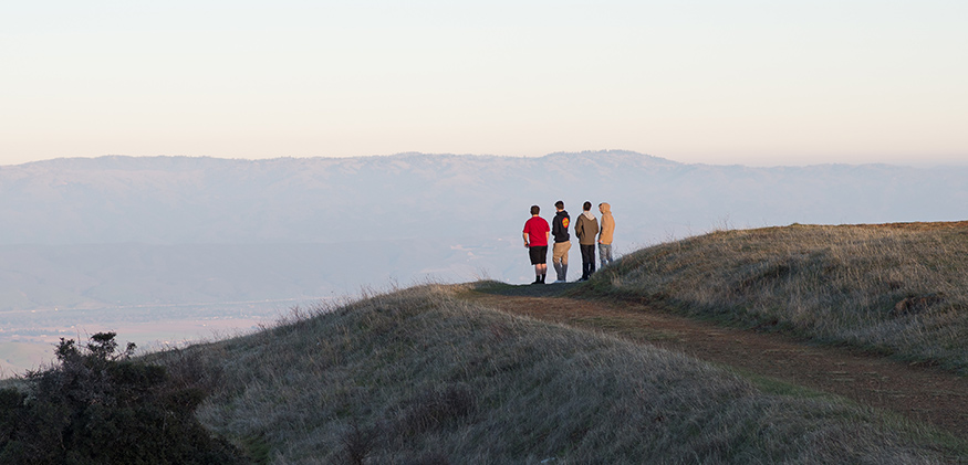 Four friends pause on a hillside hike to take in the view.