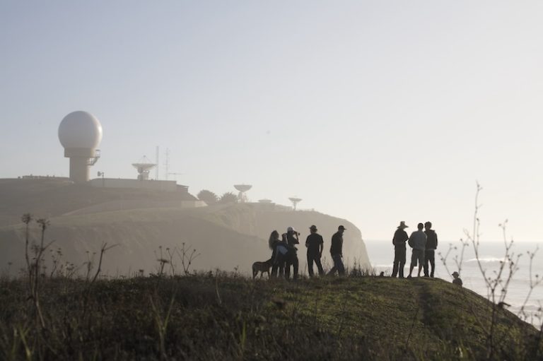 Group of people standing in the foreground, admiring the stunning view of Pillar Point at sunset